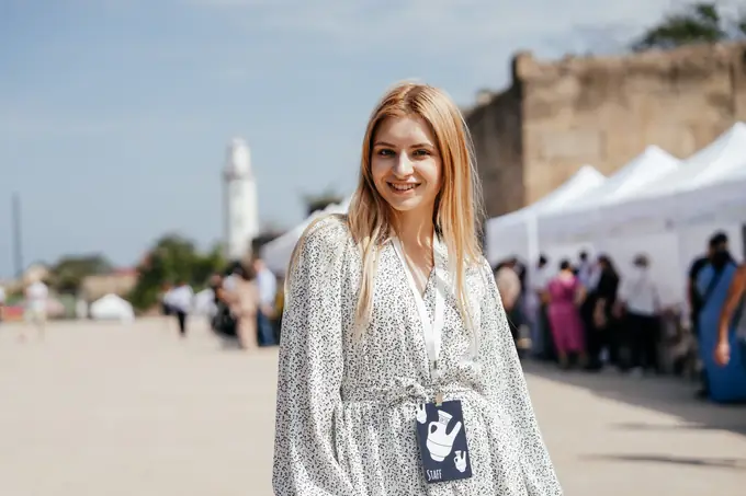 Улыбающаяся гостья фестиваля на фоне ярмарочных шатров и маяка