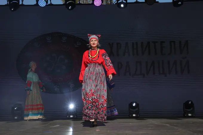 Модели в традиционных костюмах на сцене перед экраном «Хранители традиций»