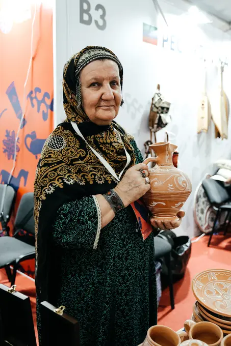 Мастерица в национальном платке держит расписной керамический кувшин
